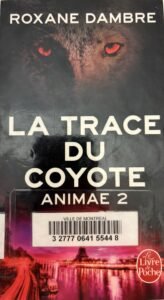 Couverture de La trace du coyote par Roxane Dambre. Une face de coyote aux yeux rouges au-dessus d'une ville.