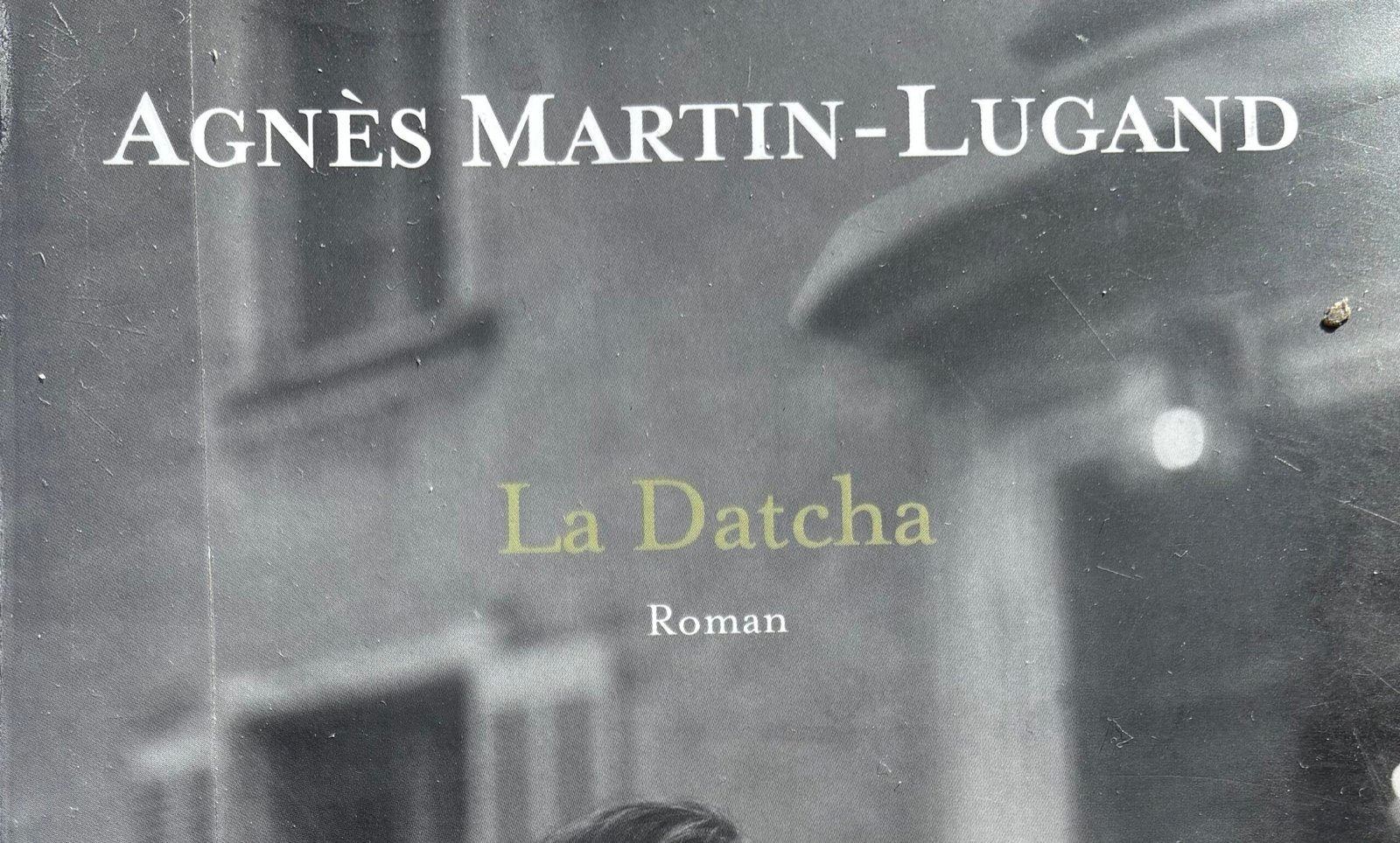 Extrait de la Couverture de La Datcha, d'Agnès Martin-Lugand : une photo en noir et blanc montre une jeune femme de dos regardant la façade d'une bâtisse