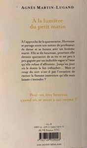Quatrième de Couverture de À la lumière du petit matin d'Agnès Martin-Lugand : en grand plan, une femme de dos la tête tournée, à la terrasse d'un café